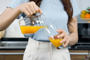 Closeup female hand pour mixed fruit and veggie smoothie from Jar into glass.