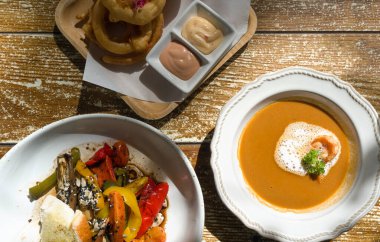 Homemade crispy onion rings, Shrimp Bisque and Grilled organic salad served on wooden table. Top View