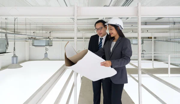 Engineer in hardhat hold the ventilation system construction plan while taking the building inspector check the cleanliness of the factory. lighting and air conditioning panels mounted on the ceiling.