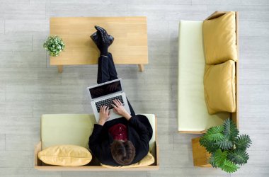 Takım elbiseli genç işadamı kanepede oturur, dizüstü bilgisayar klavyesinde yazarken ayaklarını dinlendirir. Üst Görünüm