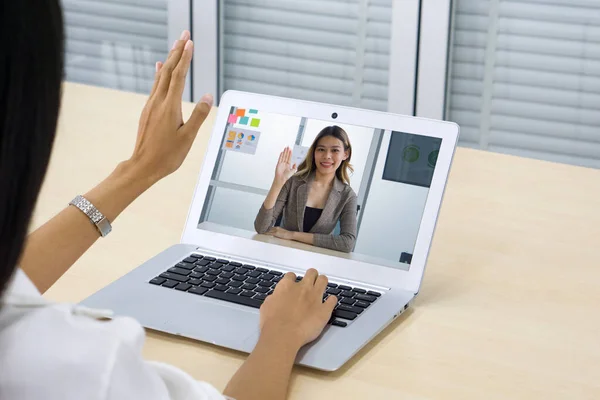 Beyaz tişörtlü genç bir kadının dizüstü bilgisayar monitörüne el sallaması, iş ortağıyla online görüşmesi. Ev kavramından çalış