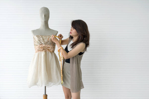 Модный дизайнерский зал. Молодая женщина портниха с помощью рулетки мера измерения размера платья на манекене.