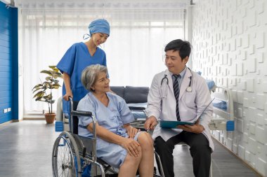 Young nurse push a wheelchair of the elderly patient while asian doctor with stethoscope and gown examine the symptom of the Total Knee Arthroplasty. Healthcare and medicine concept.