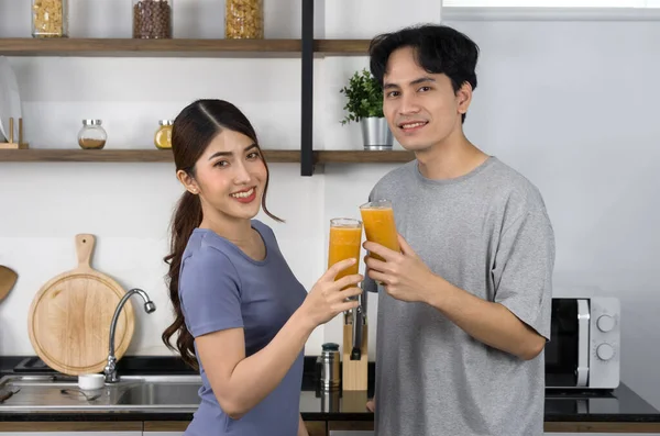 Young man in casual clothe and his girlfriend drinking mixed fruit juice and veggie smoothie. Asian lover spend morning time together in the kitchen.