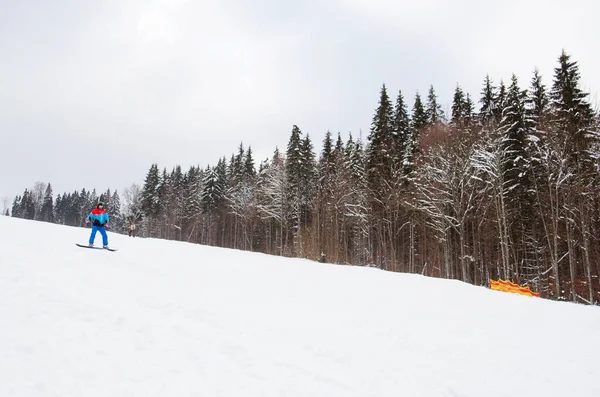 A male snowboarder descends the track next to a snowy forest. ski resort — Stock Photo, Image