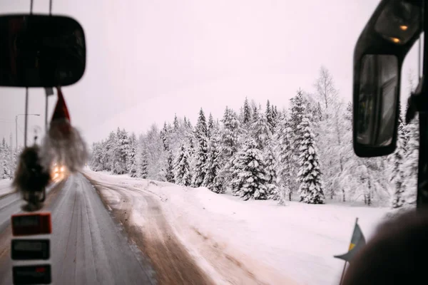 Bosque denso cubierto de nieve y un camino. Vista desde la ventana frontal del autobús — Foto de Stock