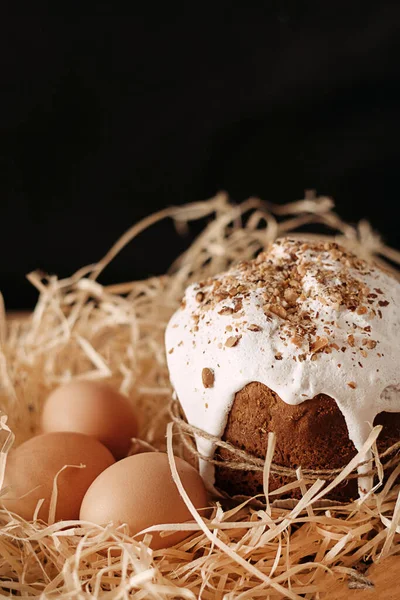 Πασχαλινό κέικ διακοσμημένο με λευκό κερασάκι δίπλα σε αυγά κοτόπουλου σε καλαμάκι σε μαύρο φόντο. — Φωτογραφία Αρχείου