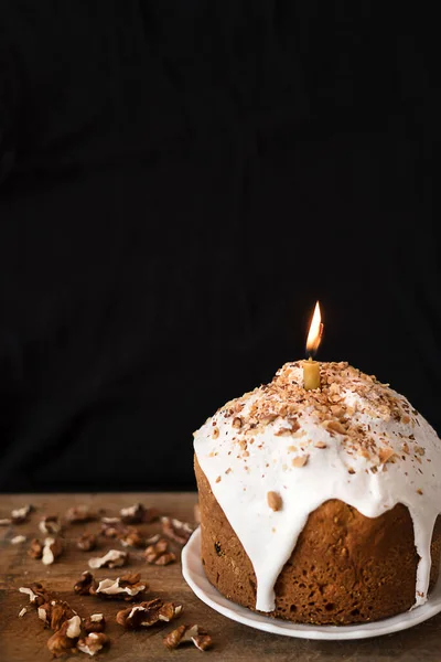 白い氷で飾られたナッツとイースターケーキ黒の背景にキャンドル. — ストック写真