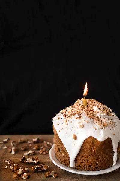 Bolo de Páscoa com nozes decoradas com cobertura branca com uma vela sobre um fundo preto. — Fotografia de Stock