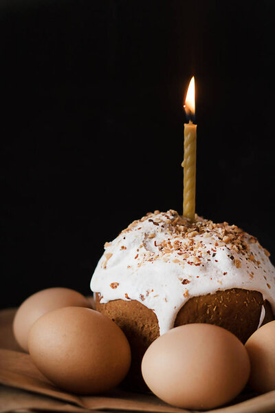 Easter cake decorated with white icing with a candle and eggs on a black background.
