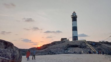 10 Eylül 2021, Mangalore, Karnataka, Hindistan. Arka planda deniz feneriyle Kapu sahilinde yürüyen bir turist. Kapu deniz feneri 1901 yılında inşa edildi ve 27 metre yüksekliğindedir.