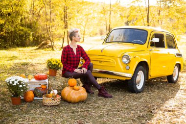 Sarı arabanın yanında gülen güzel bir kadın. Çiçekler ve balkabaklarıyla Sonbahar Park arka planında altın ağaçlarla.
