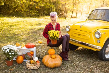 Güz parkında sarı arabanın yanında çiçekli ve balkabaklı güzel bir kadın.