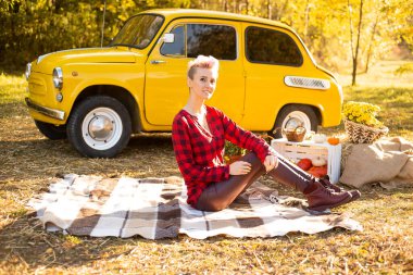 Sonbahar parkında dinlenmek, gündelik giysiler içinde bir kadın sonbahar parkında arka planda, sarı arabanın, çiçeklerin ve balkabaklarının yanında uzanmak.