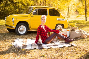 Sonbahar parkında dinlenme, sonbahar parkında arka planda, sarı araba, çiçekler ve balkabaklarının yanında battaniyeye uzanan hippi kadın.