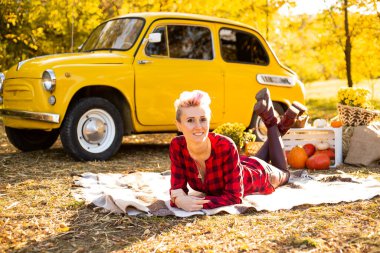 Güz parkında, arka planda, sarı arabanın, çiçeklerin ve balkabaklarının yanında, kısa saçlı şık bir yeniyetme kadın.