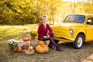 Sarı arabanın yanında gülen güzel bir kadın çiçekler ve balkabaklarıyla Sonbahar Park arka planında altın ağaçlarla