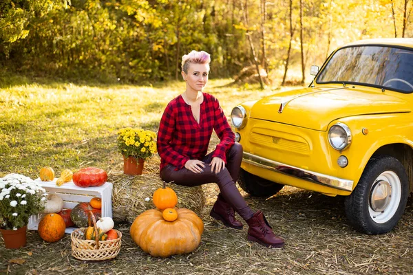 stock image hipster woman near yellow car with flowers and pumpkins in autumn park background with golden trees