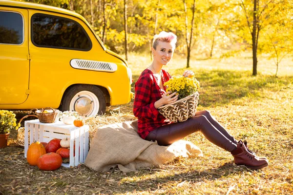 Sonbahar parkında sarı arabanın yanında çiçekli ve balkabaklı kadın sepeti.