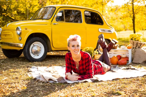 Güz parkında, arka planda, sarı arabanın, çiçeklerin ve balkabaklarının yanında, kısa saçlı şık bir yeniyetme kadın.