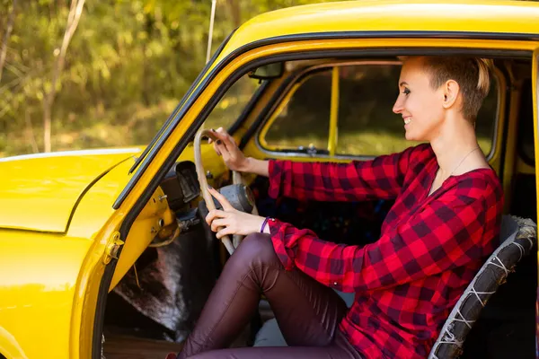 Güler yüzlü hippi kadın, sonbahar parkında arka planda altın ağaçlarla retro arabanın arkasında kısa saçlı.