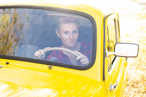 Güler yüzlü, kısa saçlı hippi kadın sonbahar parkında altın ağaçlarla arka planda retro araba kullanıyor.