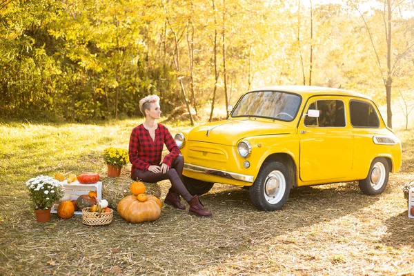 Sonbahar parkında çiçekli ve balkabaklı sarı arabalı hippi kadın altın ağaçlı arka planda