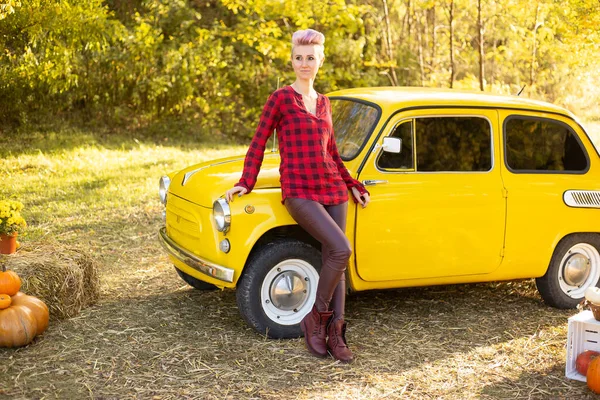 Sonbahar parkında sarı retro arabanın yanında altın ağaçlı bir hippi kadın.