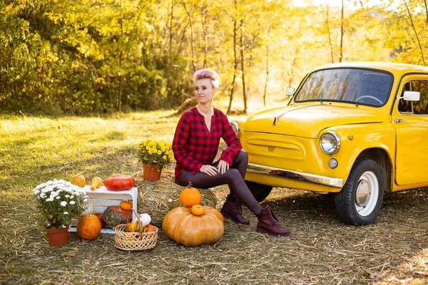 Sarı arabanın yanında gülen güzel bir kadın çiçekler ve balkabaklarıyla Sonbahar Park arka planında altın ağaçlarla