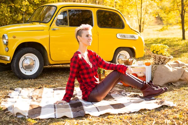 Sonbahar parkında dinlenme, sonbahar parkında battaniyeye uzanmış bir kadın sarı arabanın, çiçeklerin ve balkabaklarının yanında.