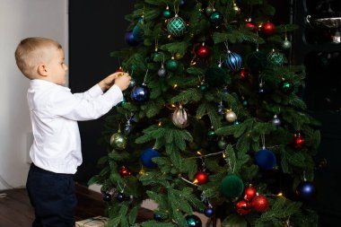 Küçük çocuk Noel süsüsüyle ağacı süslüyor.