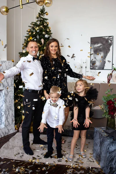 両親と幸せな子供たちの娘と息子はクリスマスに家庭でコンフェッティと遊んでいます — ストック写真