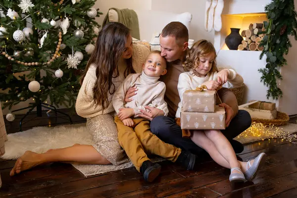 プレゼント付きの家族を愛しています 屋内の木の近くの家で床で楽しんでいる親と小さな子供 — ストック写真