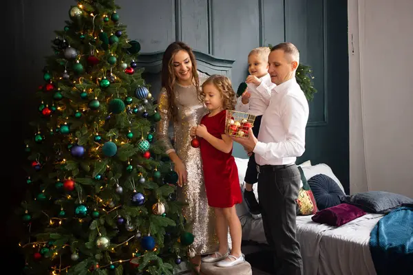 ハッピーな両親とその子供たちは屋内でクリスマスツリーを飾ります 自宅でクリスマスを待っている家族 — ストック写真
