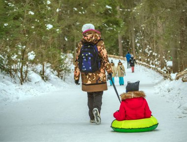 Mom is towing kite tube with a her son on the snow. Towed snow tubing. Rear view.