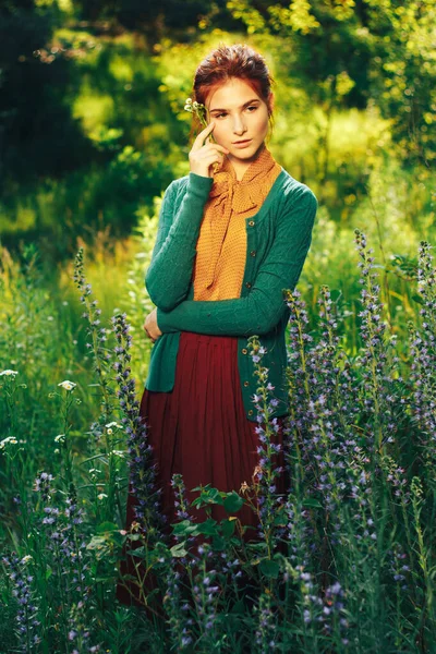 밭의 꽃들 사이에 갈색 머리카락을 가진 아름다운 소녀의 초상화. 여름 방학에 꽃이 핀다. 시골 — 스톡 사진