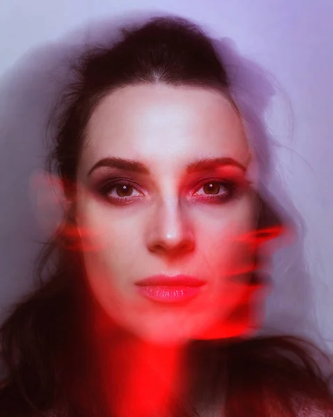 Abstract portrait of a woman with a shade of her face blurred in motion in ambient red light