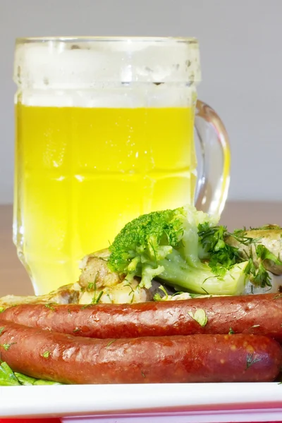 Plate with several kinds of sausages, slices of grilled meat and cauliflower, and some glass of light beer — Stock Photo, Image