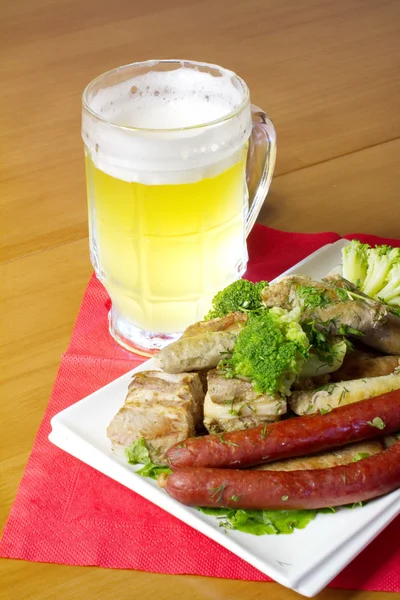Тарелка с несколькими видами колбас, ломтиками жареного мяса и цветной капусты, и стаканом светлого пива — стоковое фото