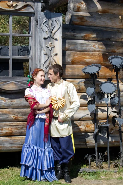 A girl and a young guy with a Russian national dress on a background of wooden houses — Stock Image A girl and a young guy with a Russian national dress on a background of wooden houses Royalty Free Stock Images