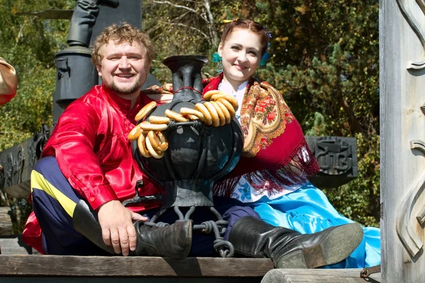 A young man and a beautiful girl in national dress sitting around iron samovar — Stock Photo, Image