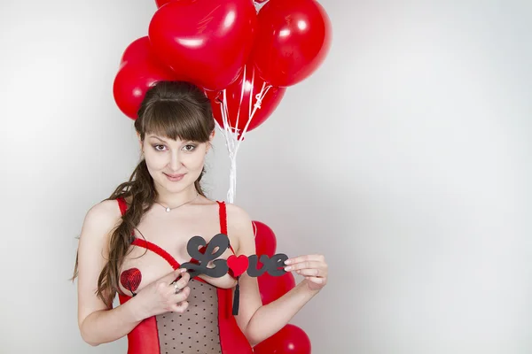 Mooi meisje in een rode jurk met sexy rode ballonnen in de vorm van hart — Stockfoto