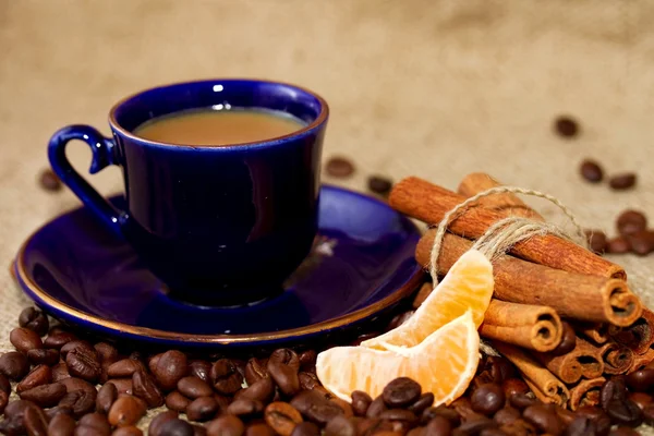 A cup of coffee with milk, coffee beans, mandarin slices and cinnamon sticks