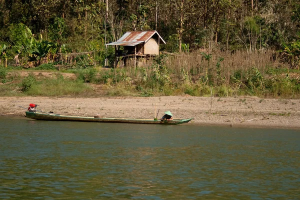 A man in a boat fishing on the background of a small bamboo house on the shore — Stock Photo, Image