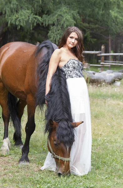 Beautiful girl in a long white skirt with a brown horse — Stock Photo, Image