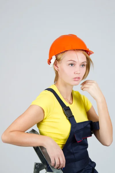Confused young girl in overalls and a helmet — Stock Photo, Image