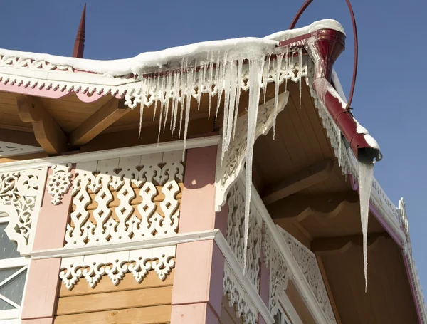 Große Eiszapfen auf dem Dach eines Holzhauses mit geschnitzten Ornamenten — Stockfoto