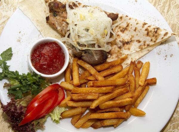 Pork shish kebab on pita bread with french fries and sauce