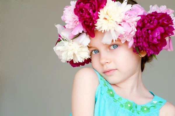 Entzückendes kleines Mädchen mit Kranz aus Pfingstrosenblumen Stockbild