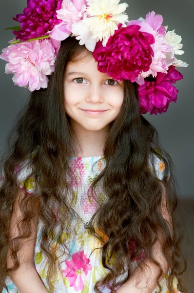 Entzückendes kleines Mädchen mit Kranz aus Pfingstrosenblumen im Atelier Stockbild